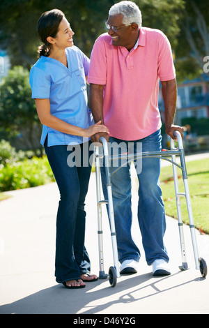 Accompagnatore aiutando Senior Uomo con telaio a piedi Foto Stock