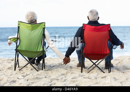 Coppia senior seduto sulla spiaggia in sedie a sdraio Foto Stock