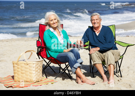 Coppia senior seduto sulla spiaggia in sedie a sdraio con picnic Foto Stock