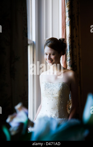 Sposa in crema senza spalline abito da sposa con capelli fino illuminata da grandi finestre a ghigliottina. Foto Stock