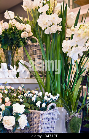 Immagine interno di negozio riempito di fiori di imitazione in grandi cestini di canna con 3 graziosi conigli in ceramica su una scrivania in background. Foto Stock