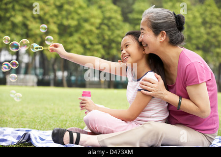 Nonna cinese con il nipote In Park a soffiare bolle Foto Stock