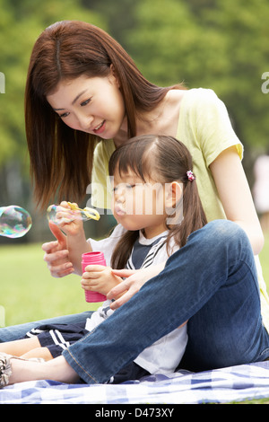 Madre cinese con la figlia nel parco a soffiare bolle Foto Stock