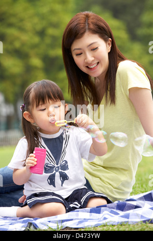 Madre cinese con la figlia nel parco a soffiare bolle Foto Stock
