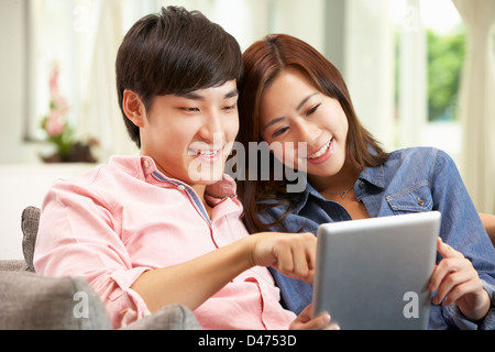 Giovani cinesi giovane con tavoletta digitale mentre vi rilassate sul divano di casa Foto Stock