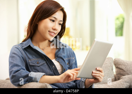 Giovane donna cinese con tavoletta digitale mentre vi rilassate sul divano di casa Foto Stock