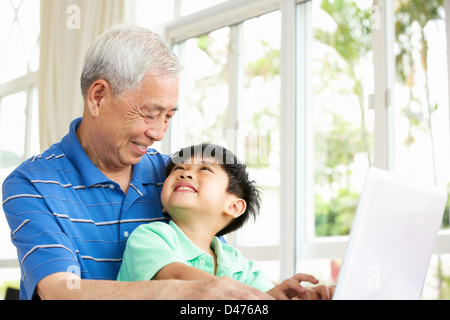 Nonno cinese e il nipote seduto alla scrivania con computer portatile a casa Foto Stock