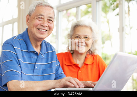 Cinese Senior giovane seduto alla scrivania con computer portatile a casa Foto Stock