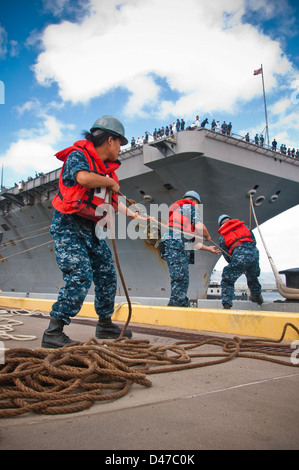 I marinai a bordo della portaerei classe Nimitz USS John C. Stennis (CVN 74) lavorano sulle linee di ormeggio mentre la nave arriva alla Joint base Pearl Harbor-Hickam. L'attività garantisce un ancoraggio sicuro e la disponibilità alle operazioni presso la base navale. Foto Stock