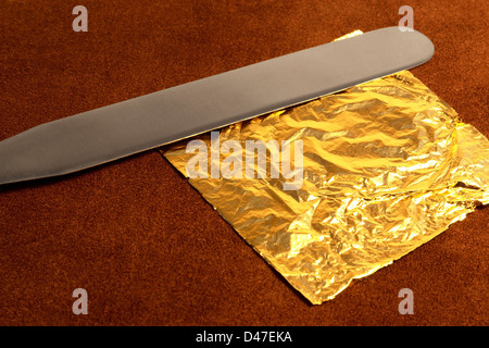 Tema di doratura con una foglia di oro battuto e lama sulla pelle marrone con superficie in ambiente caldo Foto Stock