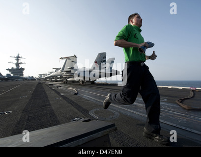 Un marinaio corre strumenti per altri marinai come loro di eseguire le operazioni di manutenzione sulla prua di una catapulta. Foto Stock