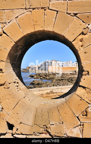 Vista attraverso l'oblò in muratura di mattoni alla costa rocciosa disseminata di fronte alla fortificata c-16 città portoghese di Essaouira, Marocco Foto Stock