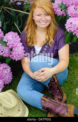 Ragazza sorridente accanto a viola i fiori delle ortensie, dai capelli rossi diciottenne adolescente. Foto Stock