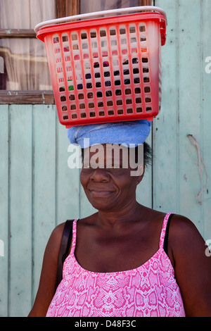 La donna da Vieux Fort Village, St Lucia portando i suoi messaggi in un rosso scatola di plastica e sulla sua testa Foto Stock