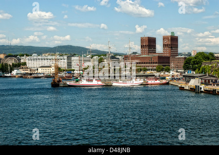 Barche ormeggiate nel porto di Oslo riflettono il tardo pomeriggio di sole circondato da antichi e moderni edifici intorno alla banchina Foto Stock