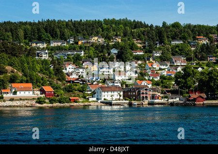 Un piccolo paese sulle rive del Oslofjord con bianco pristine case guardando fuori dal tra gli abeti nel tardo pomeriggio di sole Foto Stock