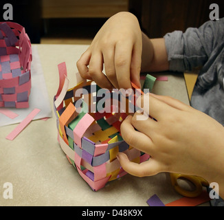 Arti e mestieri con le mani di un bambino la creazione di un cestello in costruzione della carta come un simbolo di arte istruzione in scuole o altre attività creative per i bambini. Foto Stock