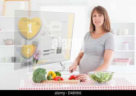 Donna incinta di preparare la cena tramite interfaccia ologramma Foto Stock