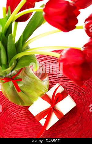 Immagine del bellissimo rosso fresco bouquet di tulipani in vaso di vetro e un po' di scatola regalo bianca decorata con nastro sulla tabella, Foto Stock