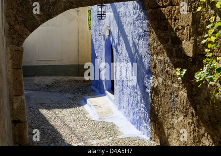 Rodi. La Grecia. Un abbastanza soleggiato strette in ciottoli vicolo di pietra con archi e blu e pareti di colore giallo. Foto Stock