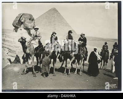 Una fotografia del 1924 di turisti che cavalcano cammelli vicino alle piramidi di Giza e alla grande Sfinge in Egitto. L'immagine cattura il paesaggio iconico e il turismo culturale in Egitto. Foto Stock