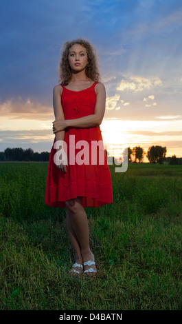 Foto di bella donna in abito rosso permanente sulla sunset Foto Stock