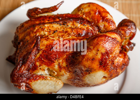 Un intero pollo arrosto su una piastra bianca e bambù placemat Foto Stock