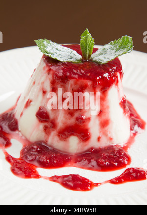 Panna cotta con un fresco e confettura di fragole decorate con foglie di menta e zucchero in polvere Foto Stock