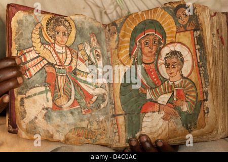 Una chiesa ortodossa etiope prete possiede un libro che mostra immagini separate di St George e la Vergine Maria con il giovane Gesù Cristo Foto Stock