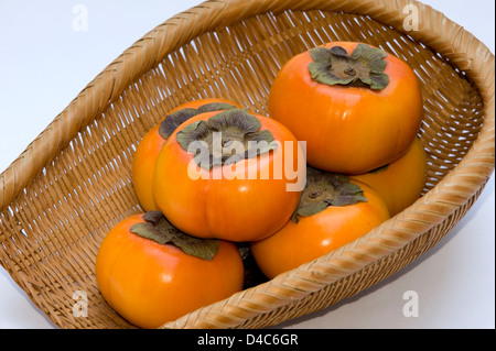 Un cesto di vimini contenenti freschi giapponese 'kaki' persimmon frutta. Foto Stock