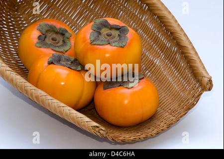 Un cesto di vimini contenenti freschi giapponese 'kaki' persimmon frutta. Foto Stock