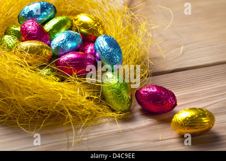 Uova di pasqua di cioccolato in giallo nido su un tavolo di legno dello sfondo. Composizione di vacanza Foto Stock