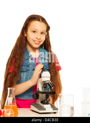 Carino brunet ragazza con i capelli lunghi nel laboratorio di chimica classe con microscopio con microscopio e provette per la prova sul tavolo, isolato su bianco Foto Stock