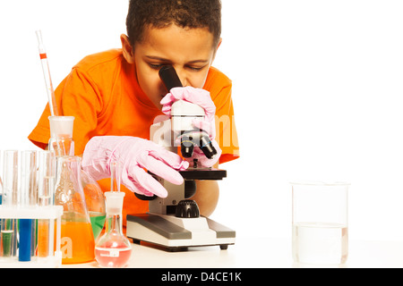 Carino black boy con capelli corti in laboratorio di chimica classe con microscopio e provette per la prova sul tavolo, isolato su bianco Foto Stock