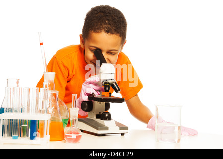 Grave 8 anni black boy con capelli corti in laboratorio di chimica classe con microscopio e provette per la prova sul tavolo, isolato su bianco Foto Stock