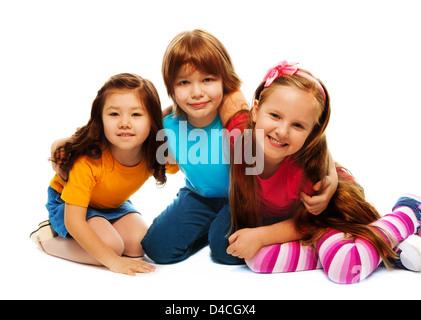 Gruppo di tre bambini, due ragazze e ragazzi insieme, asiatici e caucasici, Felice costeggiata, seduto isolato su bianco Foto Stock