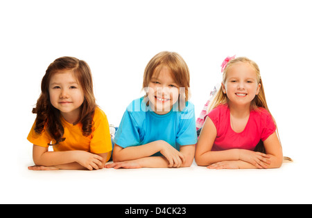 Tre bambini felici, ragazzo e due ragazze la posa sul pavimento in una linea insieme a sorridere e ridere, isolato su bianco Foto Stock