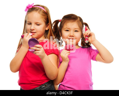 Closeup ritratto di due ragazze e caucasici Asian a giocare per essere grande come la madre e la spazzolatura che compongono il viso, isolato su bianco Foto Stock