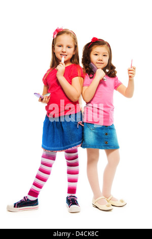 Due ragazze e caucasici Asian a giocare per essere grande come sorelle più anziane e spazzolatura che compongono il viso, isolato su bianco a piena lunghezza ritratto Foto Stock
