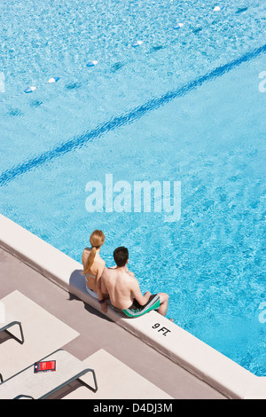 Una giovane coppia di indossare il costume da seduto sul bordo di una piscina. Foto Stock