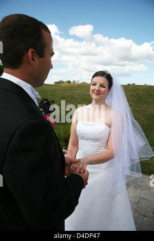 Lo sposo di mettere l'anello di matrimonio su sposa Foto Stock