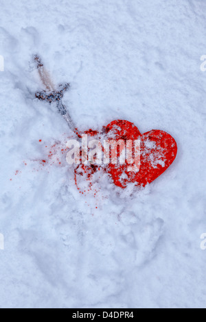 Una coperta di neve nel cuore con un pugnale e sangue Foto Stock