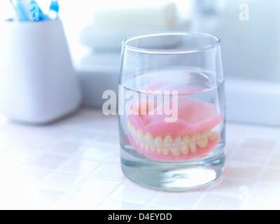 Close up di dentiere immersione in un bicchiere di acqua Foto Stock