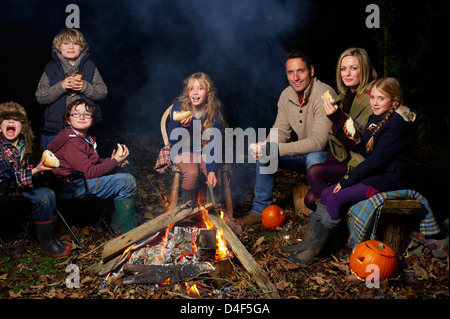 Famiglia di mangiare intorno al fuoco di notte Foto Stock