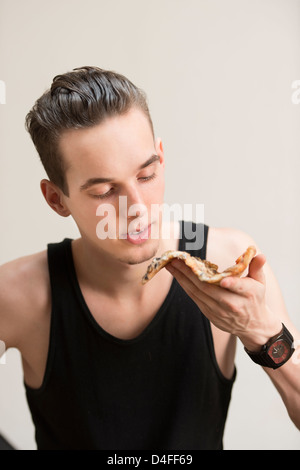 Giovane uomo adulto che indossa un serbatoio nero superiore e mangiare la pizza Foto Stock