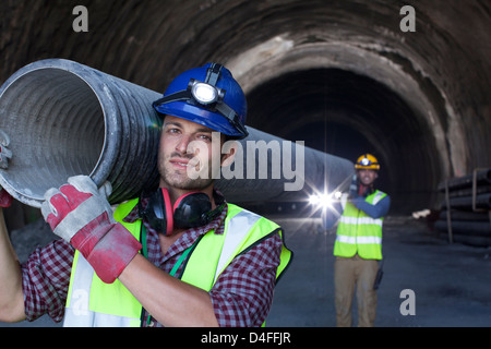 I lavoratori che trasportano un lungo tubo nel tunnel Foto Stock