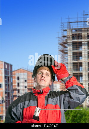 L'uomo in abiti da lavoro e una maschera del saldatore contro un edificio di nuova costruzione Foto Stock