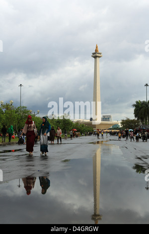 Due donne musulmane a piedi nella parte anteriore del Monas (monumento nazionale) in un giorno di pioggia a Jakarta, Indonesia Foto Stock