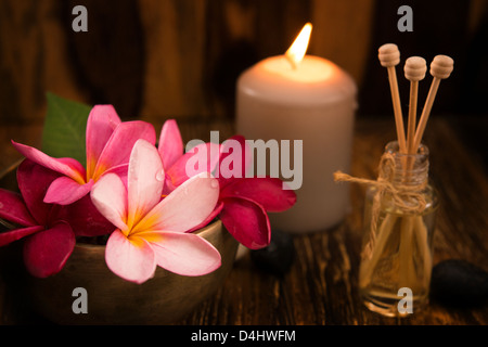 Wellness e spa concept con candele, fiore di frangipani, legno di sandalo e rattan bastoni su lettino da massaggio. Foto Stock