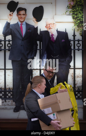 Un imprenditore e lady trasportare caselle sotto un poster per la Charles Tyrwhitt menswear outfitters a Liverpool Street nel centro di Londra, capitale il cuore del suo quartiere finanziario - una buona posizione per abiti e businesswear. Una coppia di inglesi alzare i loro Bowler Hats in un gesto da una precedente era, un bygone gentiluomo come tradizione. Quando cappelli detto molto del tuo status sociale, un riepilogo della vostra posizione nel sistema di classe. Nel XXI secolo tuttavia il cappello è in gran parte un capo di abbigliamento da indossare solo per estreme di freddo o di caldo. Foto Stock